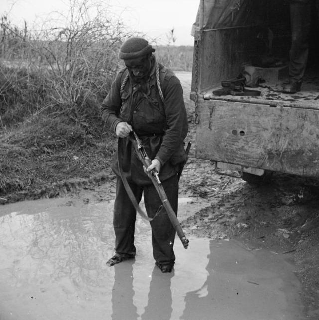 <p class='eng'>Pte. W. Balfour of Aberdeen, already soaked to the skin, stands in a puddle working the bolt of his rifle.<br />Taken by Sgt. Mott. 30.12.43. © IWM NA 10444</p>