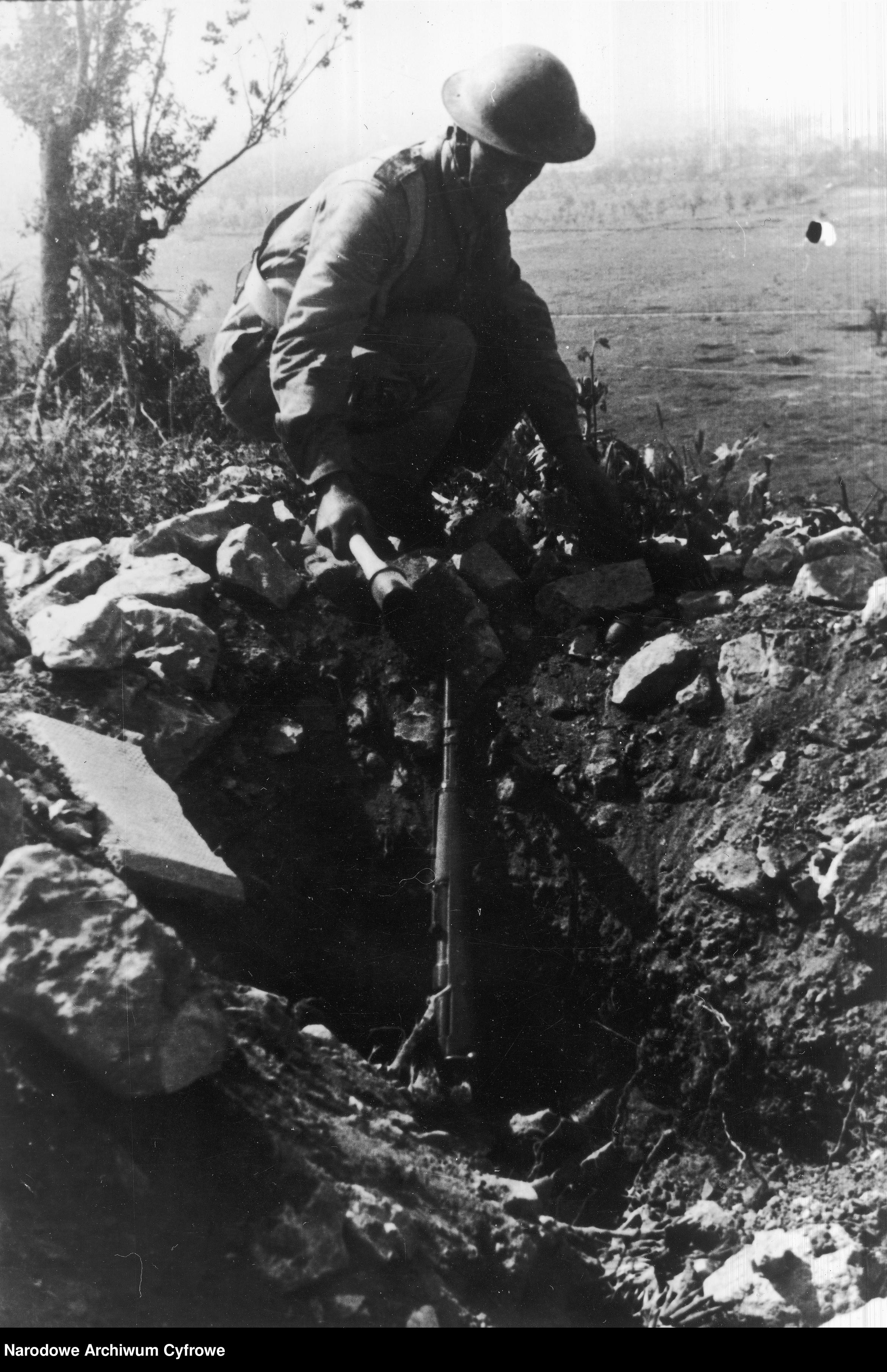 <p class='eng'>1944/05<br />One of the German defense positions. There is a Kar98k rifle in the pit and the soldier is holding a Stielhandgranate in his hand.<br />NAC 3/24/0/-/457/14</p>