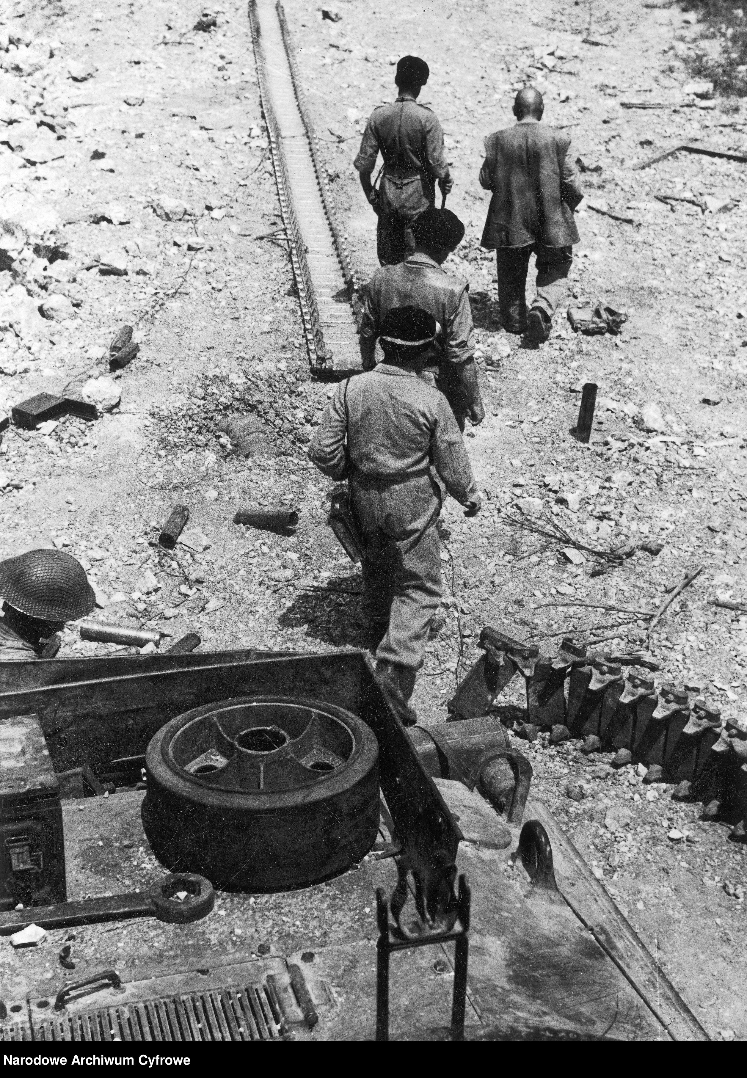 <p class='eng'>1944/05/24 - 1944/05/25<br />Soldiers replacing a broken track on the M4 Sherman tank. General Bronisław Rakowski (on the left) and Lt. Col. Władysław Bobiński (on the right) are walking side by side.<br />NAC 3/24/0/-/459/7</p>